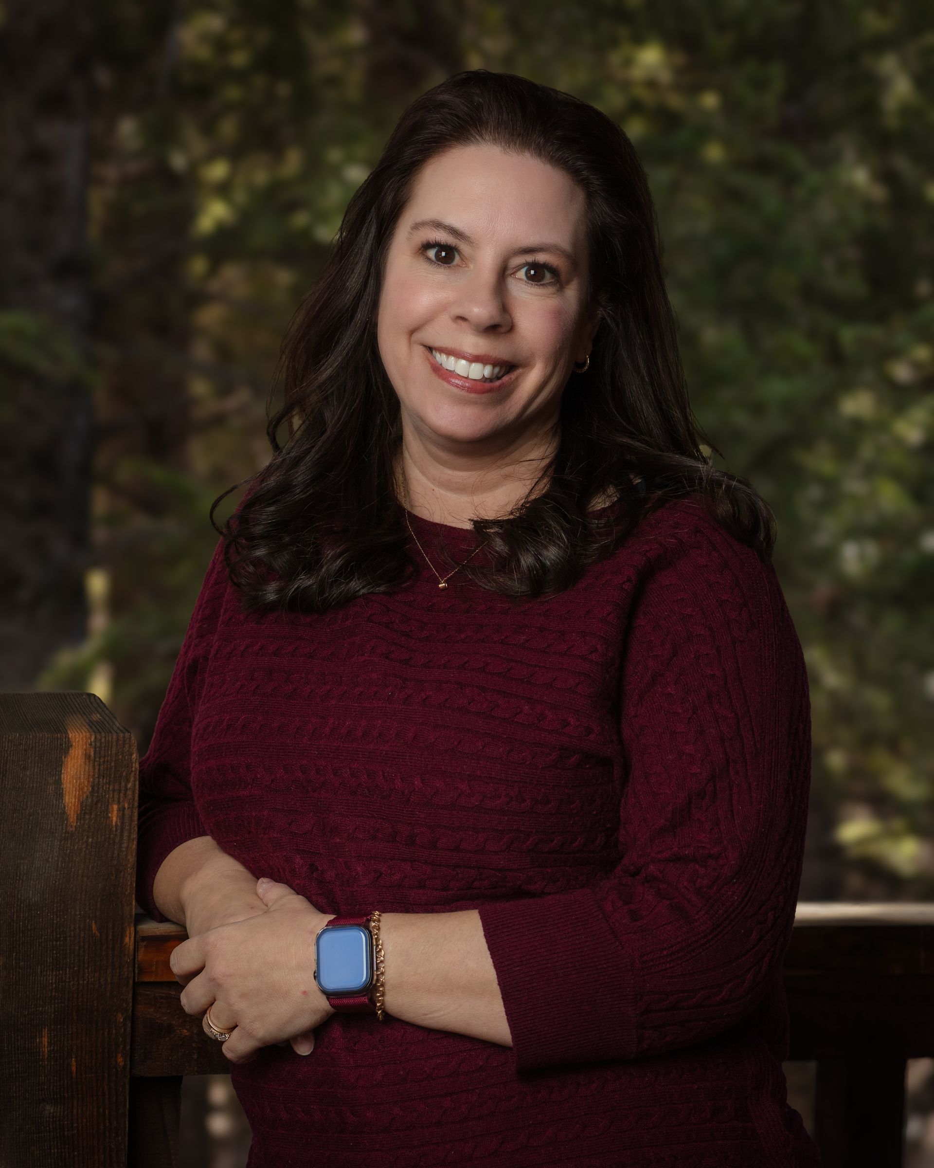 A woman wearing a maroon sweater and a blue watch is smiling for the camera.