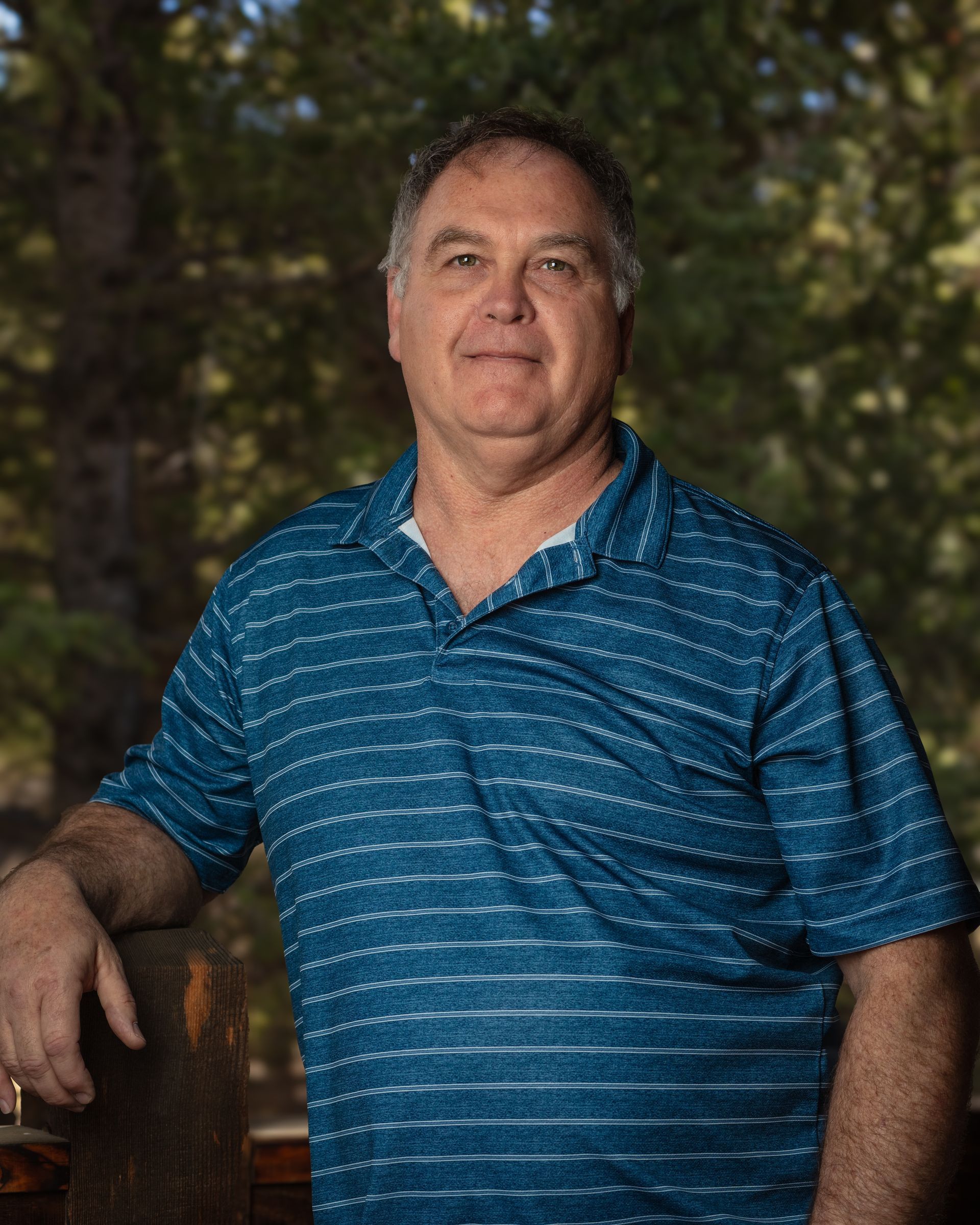 A man in a blue striped shirt is standing next to a wooden railing.