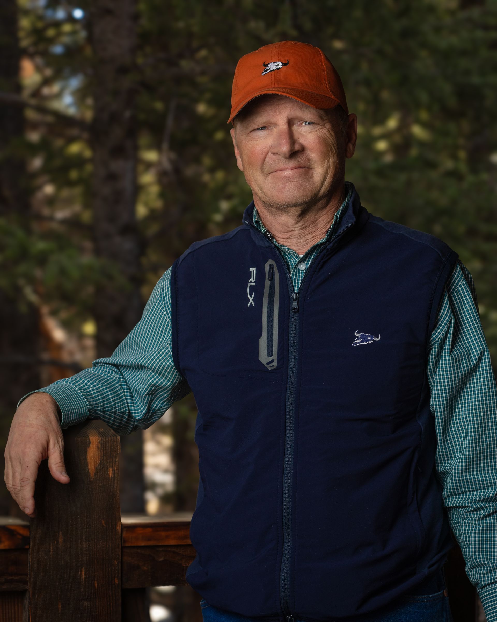 A man wearing a blue vest and an orange hat is leaning against a railing.