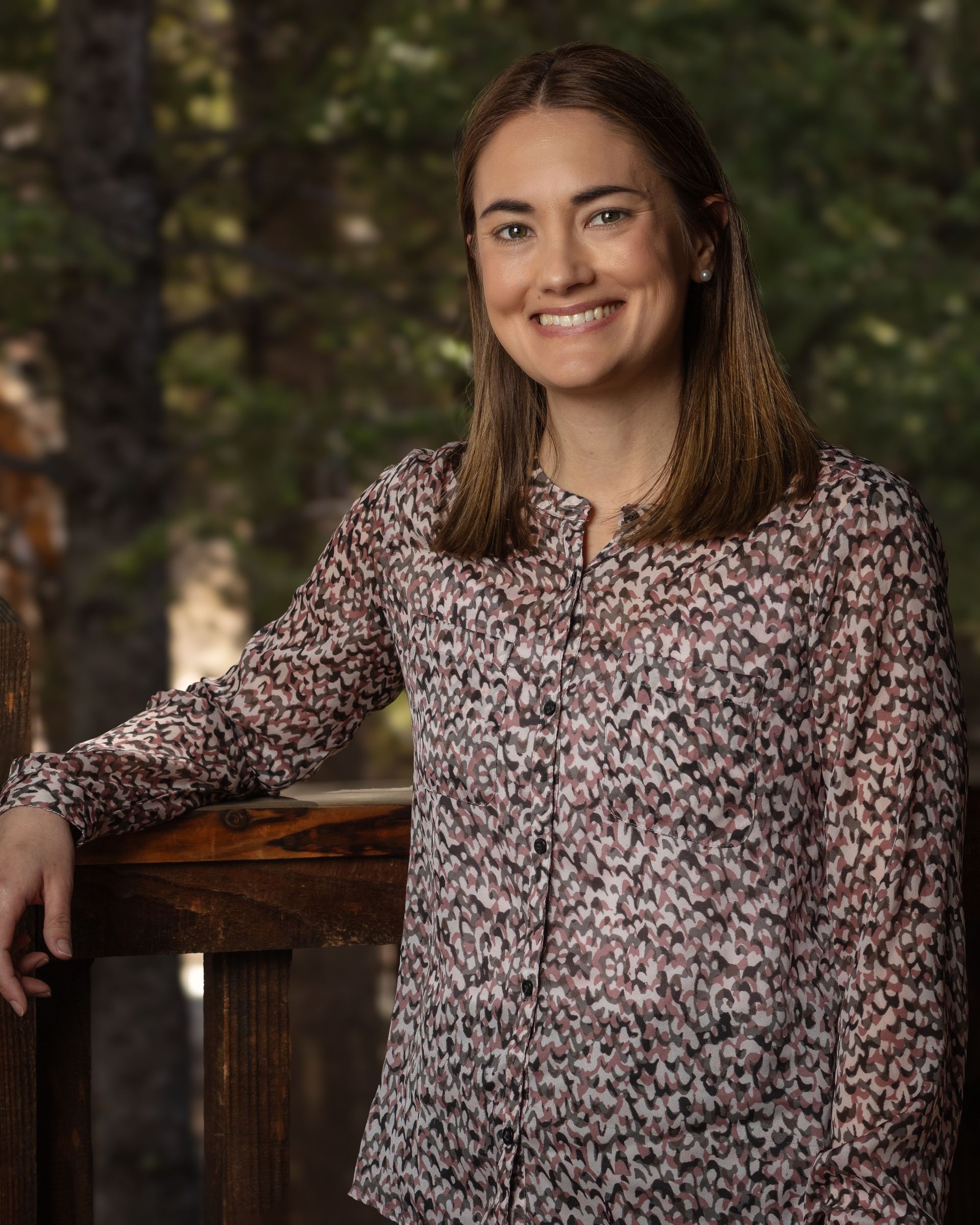 A woman in a floral shirt is standing next to a railing and smiling.