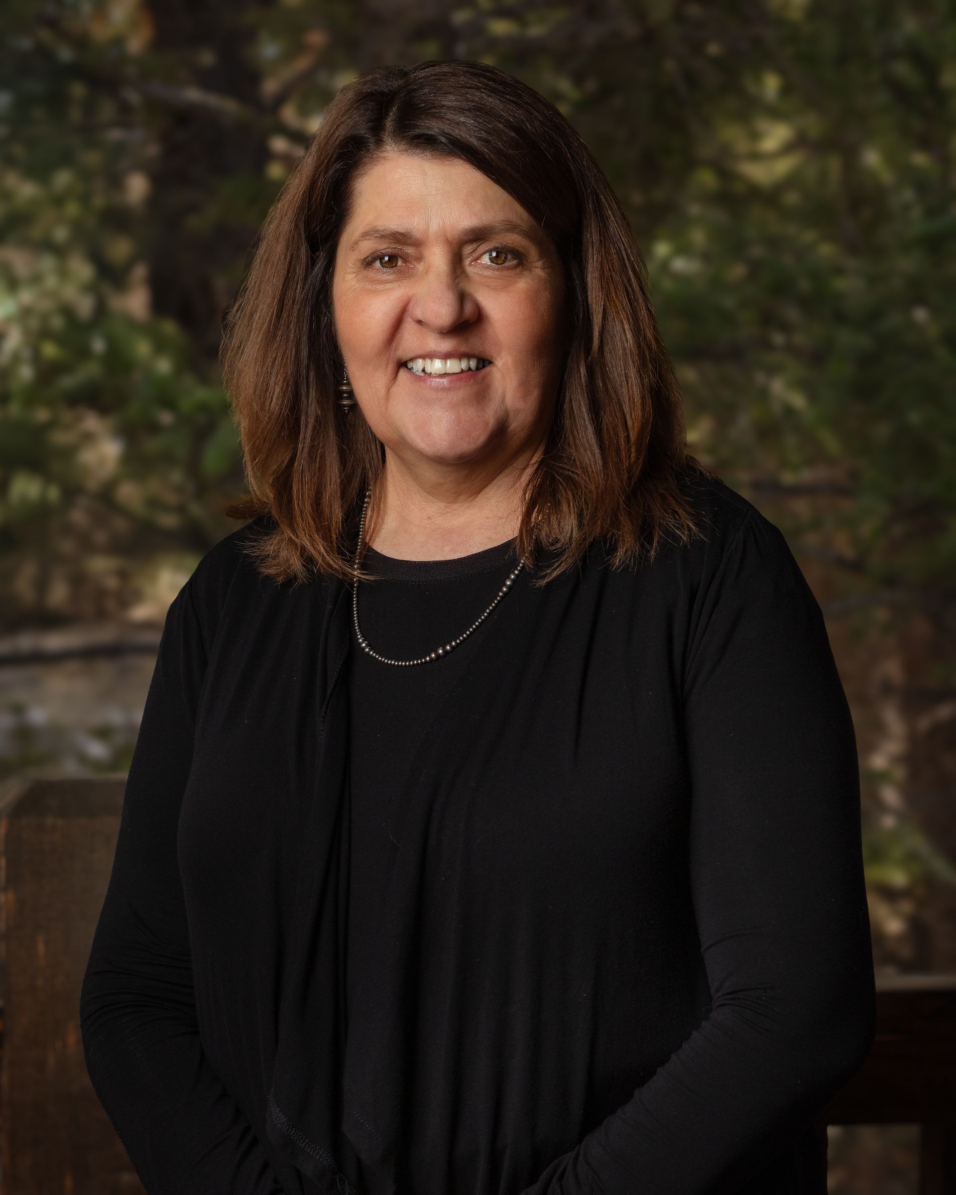 A woman in a black shirt and necklace is smiling for the camera.