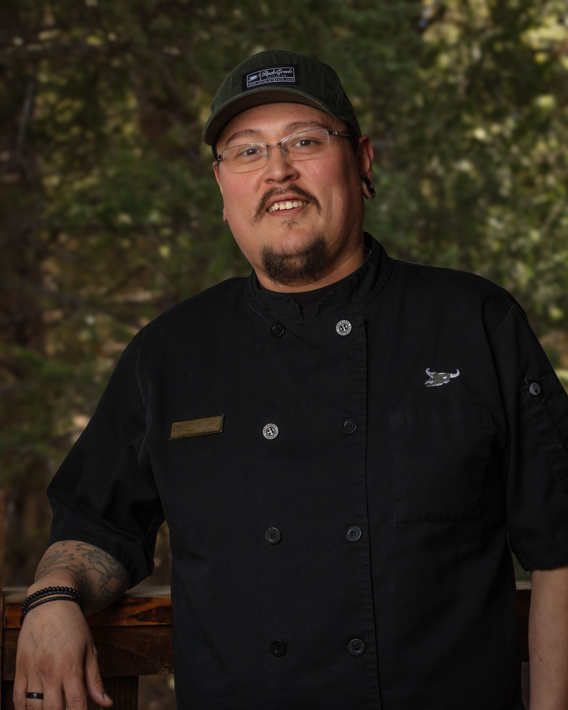A man wearing a black chef 's jacket and a hat is standing next to a railing.