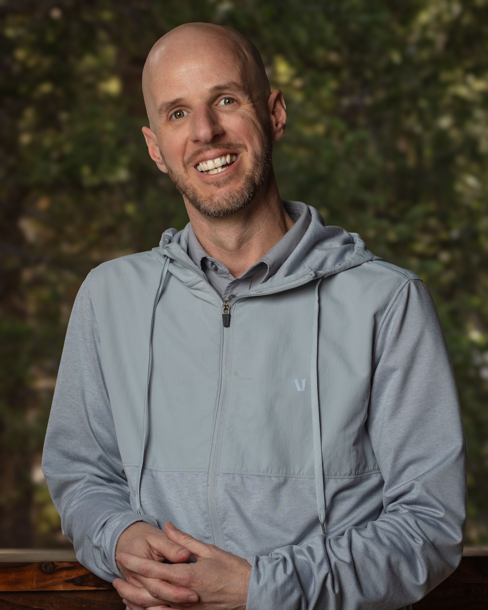 A bald man with a beard is wearing a blue hoodie and smiling.