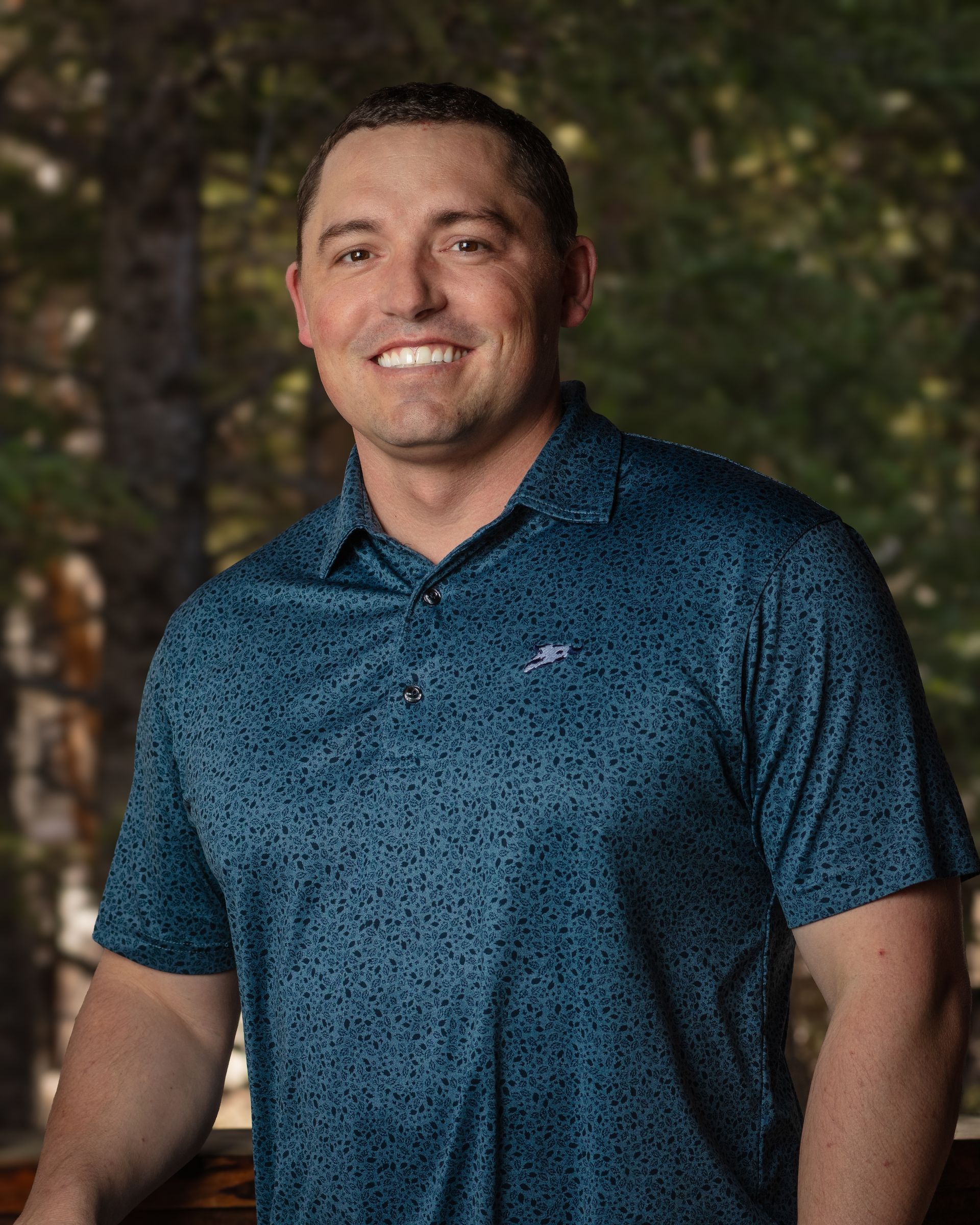 A man in a blue shirt is smiling for the camera while standing on a balcony.