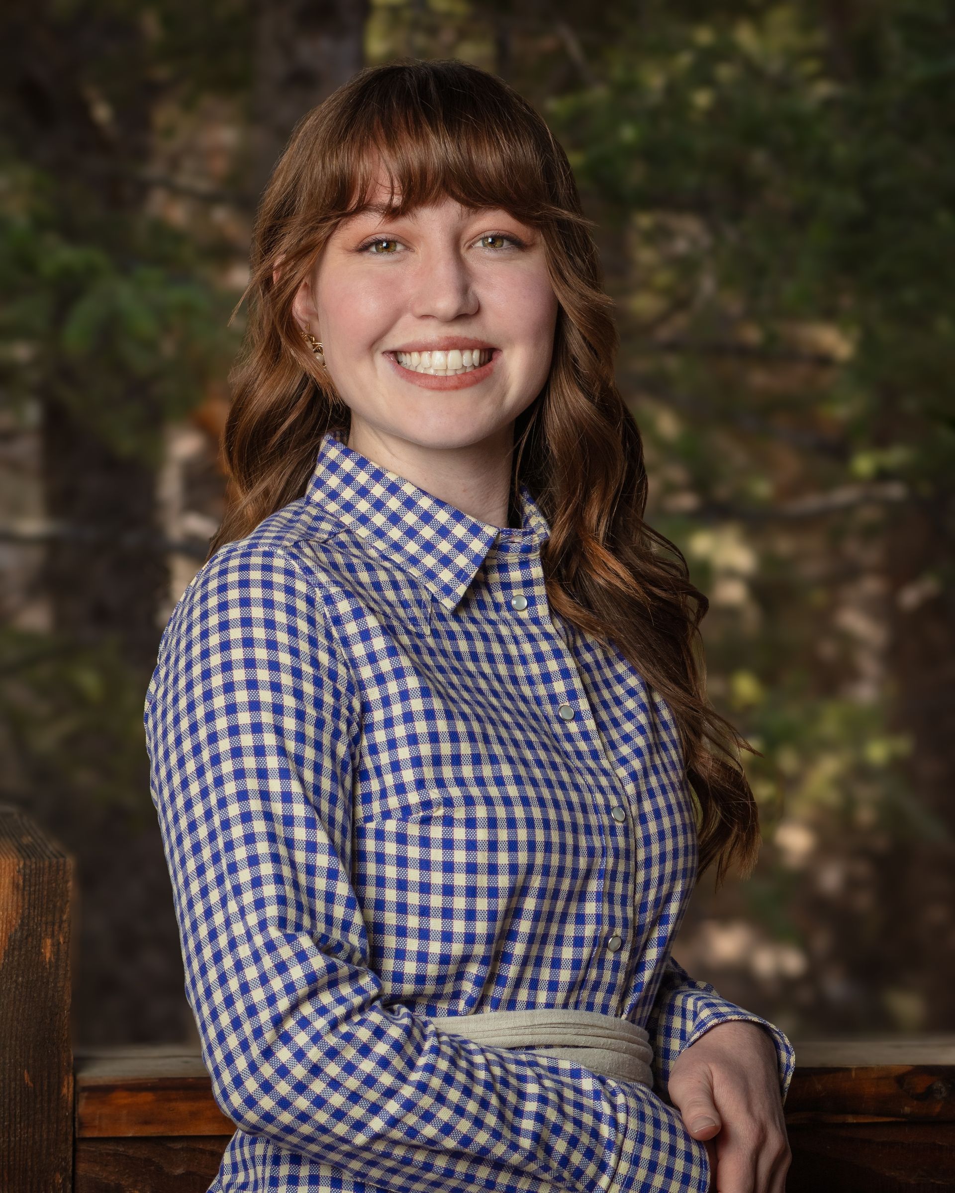 A young woman in a blue and white plaid shirt is smiling for the camera.
