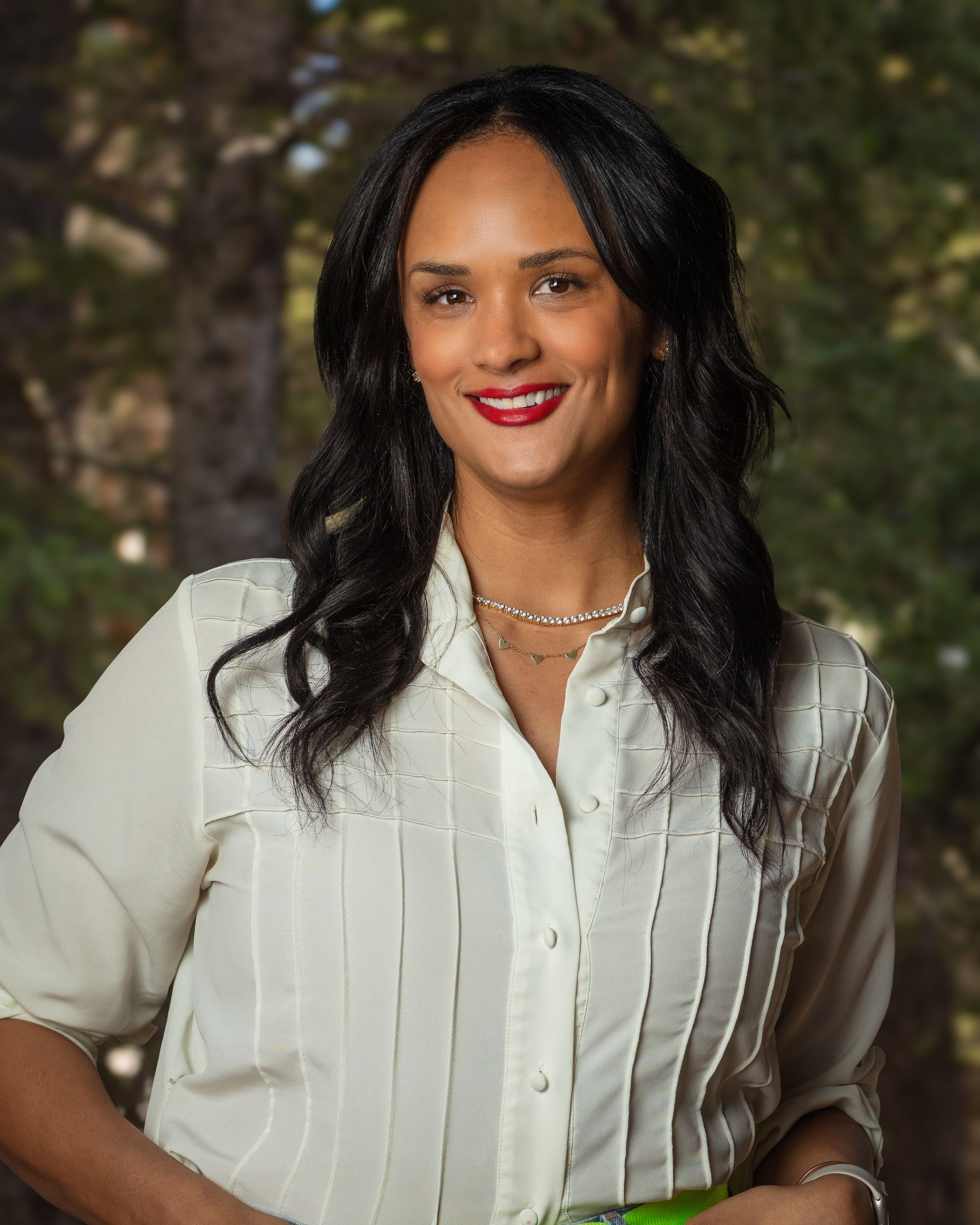 A woman wearing a white shirt and a necklace smiles for the camera