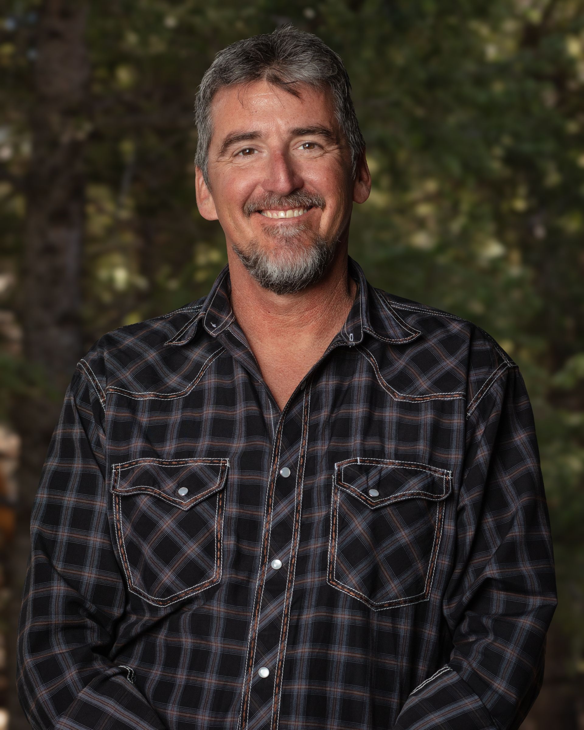 A man with a beard is wearing a plaid shirt and smiling.