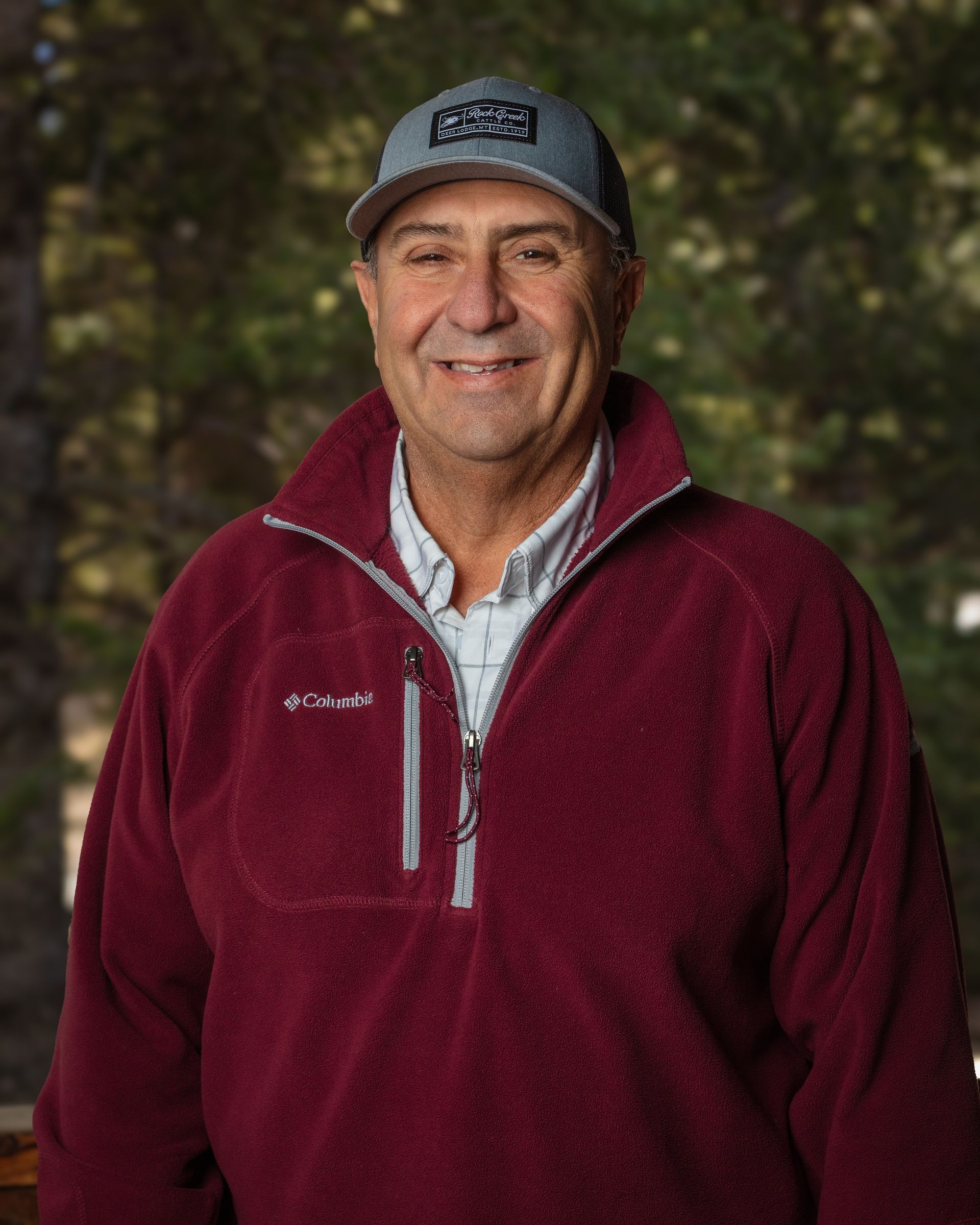 A man wearing a red jacket and a hat is smiling for the camera.