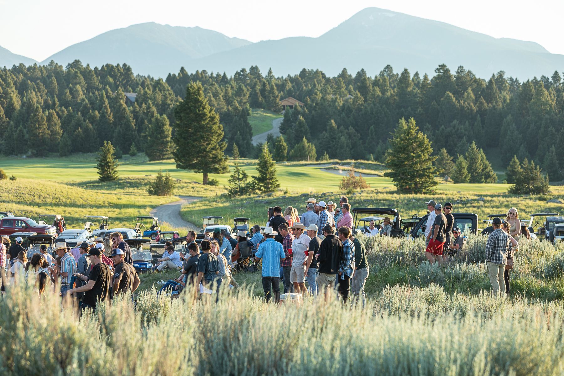 A large group of people are standing in a field with mountains in the background.