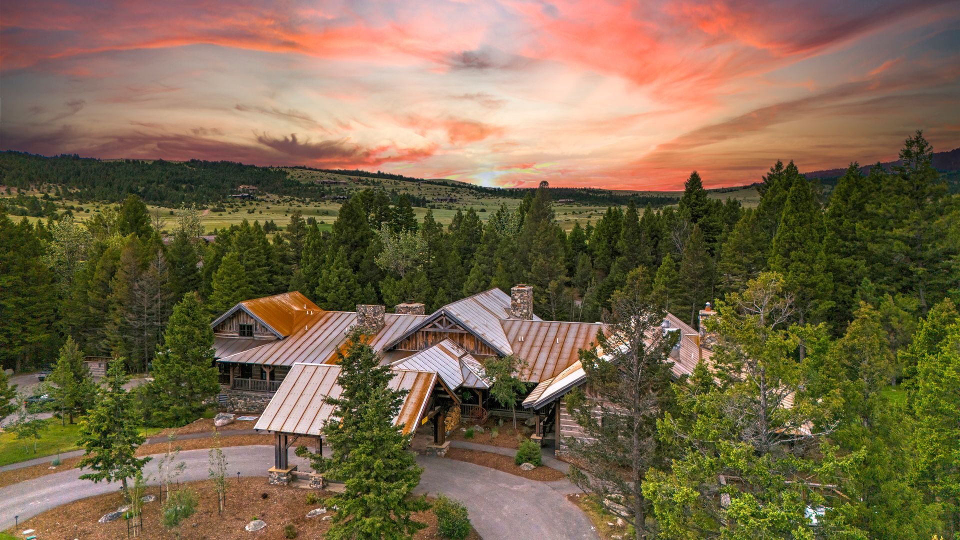 An aerial view of a large house in the middle of a forest at sunset.
