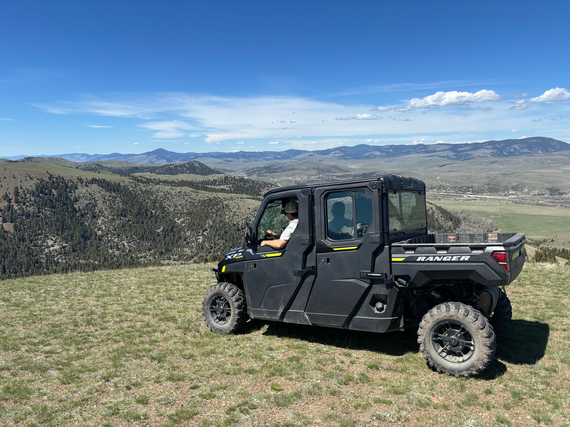 A man is driving a polaris ranger on top of a grassy hill.
