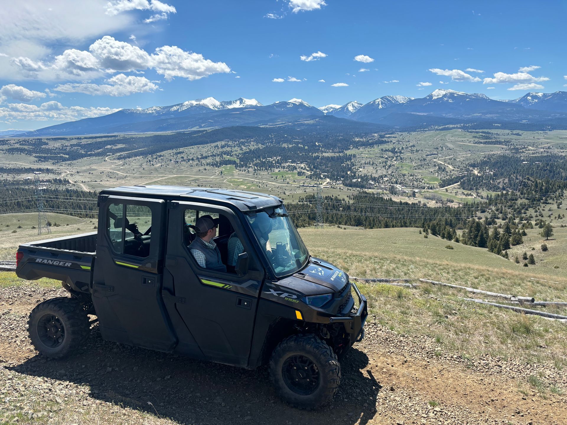 A black atv is parked on top of a dirt hill with mountains in the background.