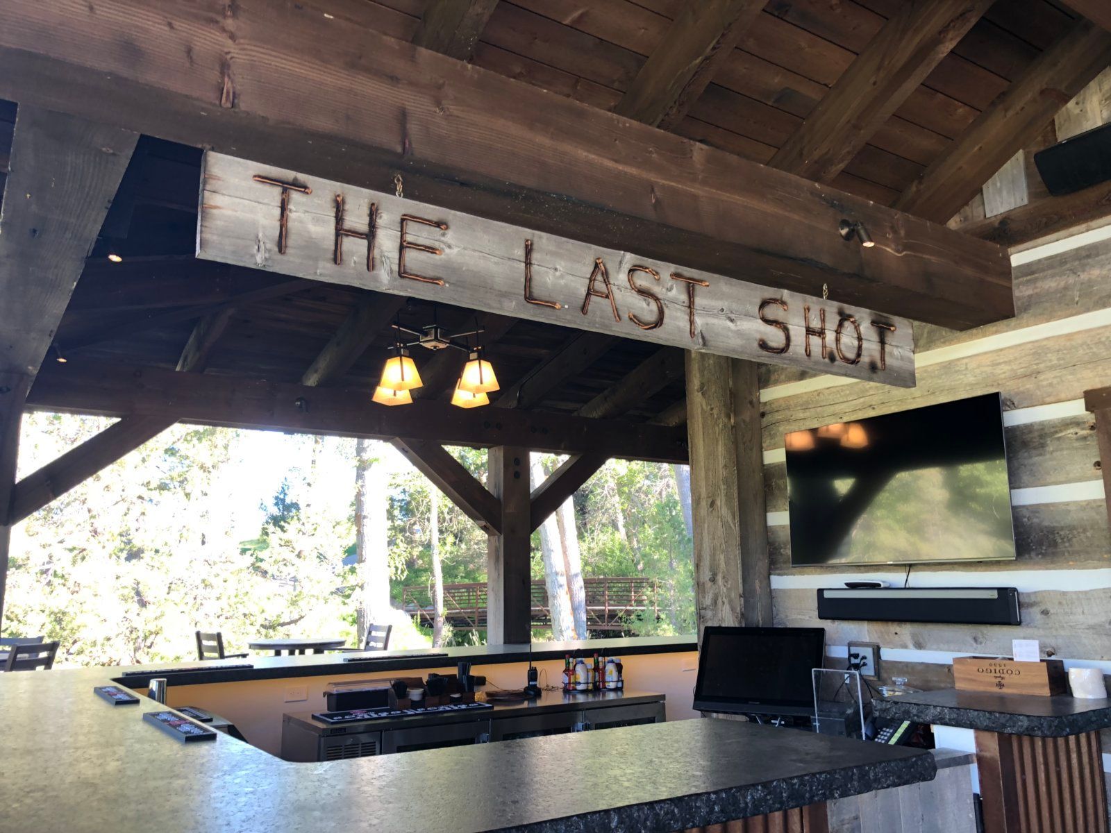 A wooden sign hangs from the ceiling above a bar.