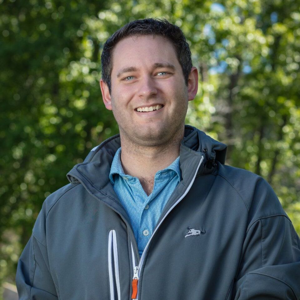 A man wearing a gray jacket and a blue shirt is smiling for the camera.
