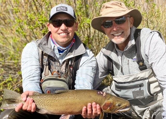 Two men are holding a large brown trout in their hands.