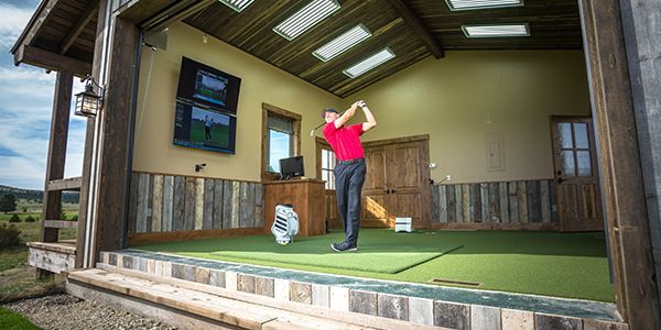 A man is swinging a golf club in a golf simulator.