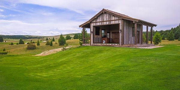 A small wooden building is sitting in the middle of a lush green field.