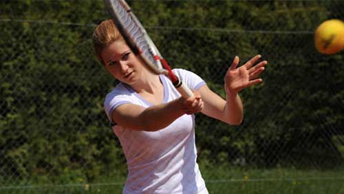 A woman is swinging a tennis racket at a tennis ball.
