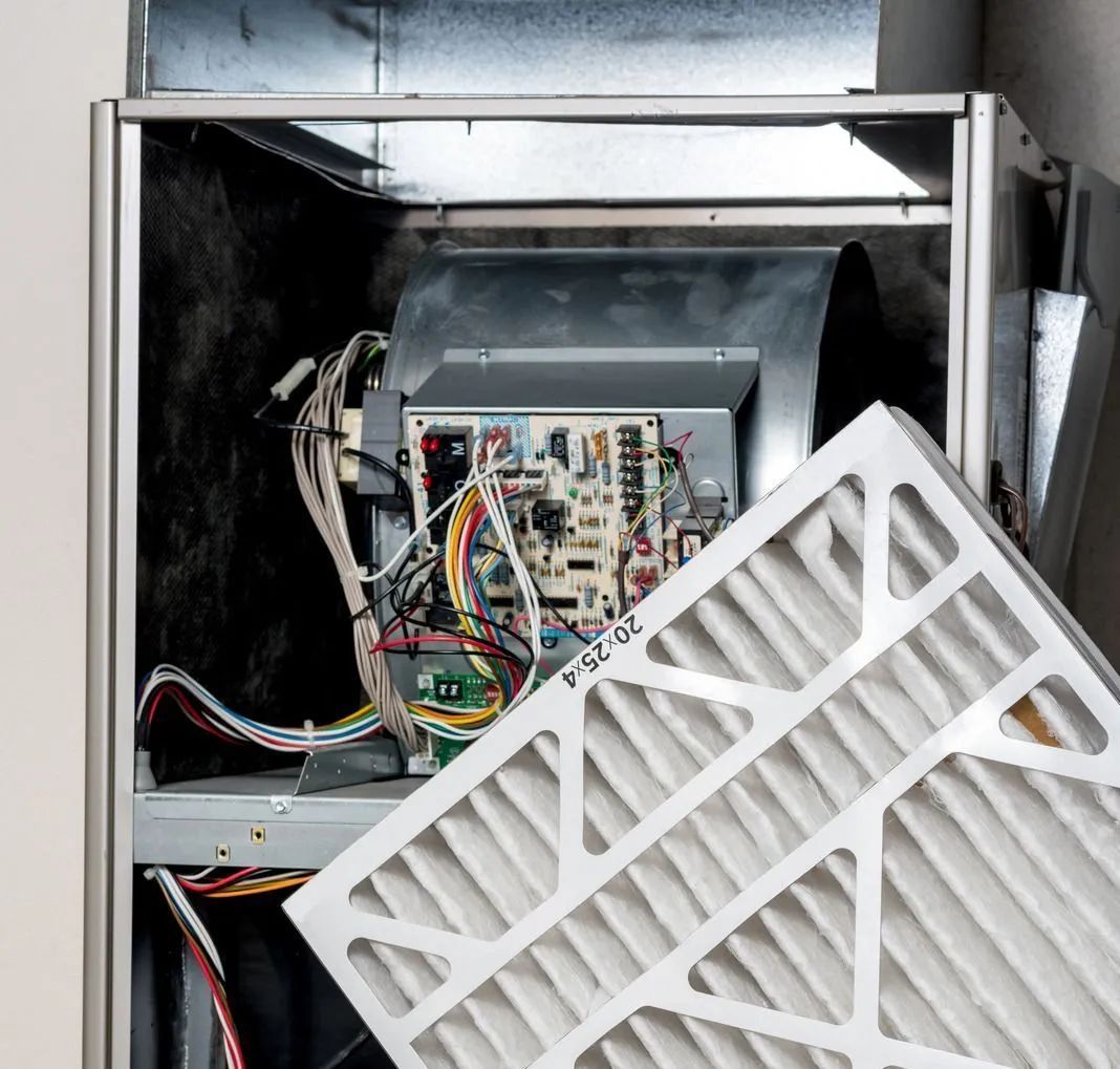 Furnace with open door, showing circuit board and a new air filter being inserted.