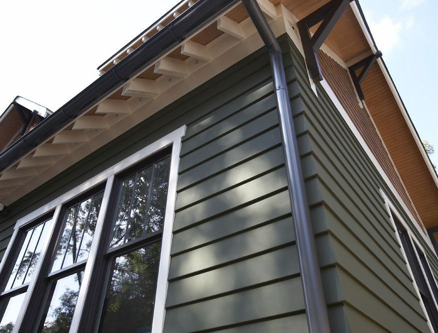 Green siding and black-framed windows on a house with brown trim and gutters.