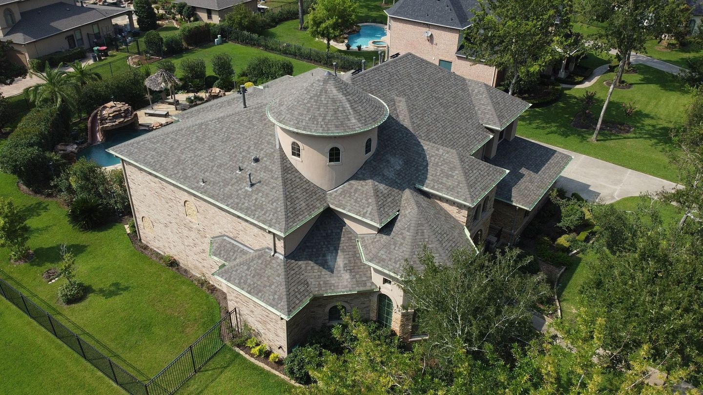 Aerial view of a stone house with a gray roof, green lawn, and a swimming pool in the backyard.