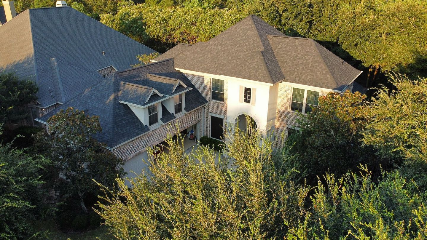 Large multi-story house with dark gray roof, surrounded by green trees.