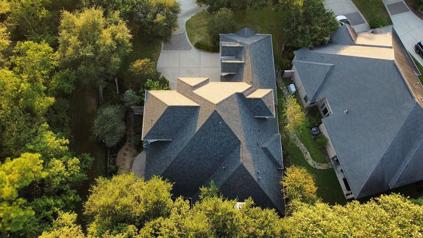 Overhead view of a multi-gabled roof house surrounded by trees in a suburban setting.