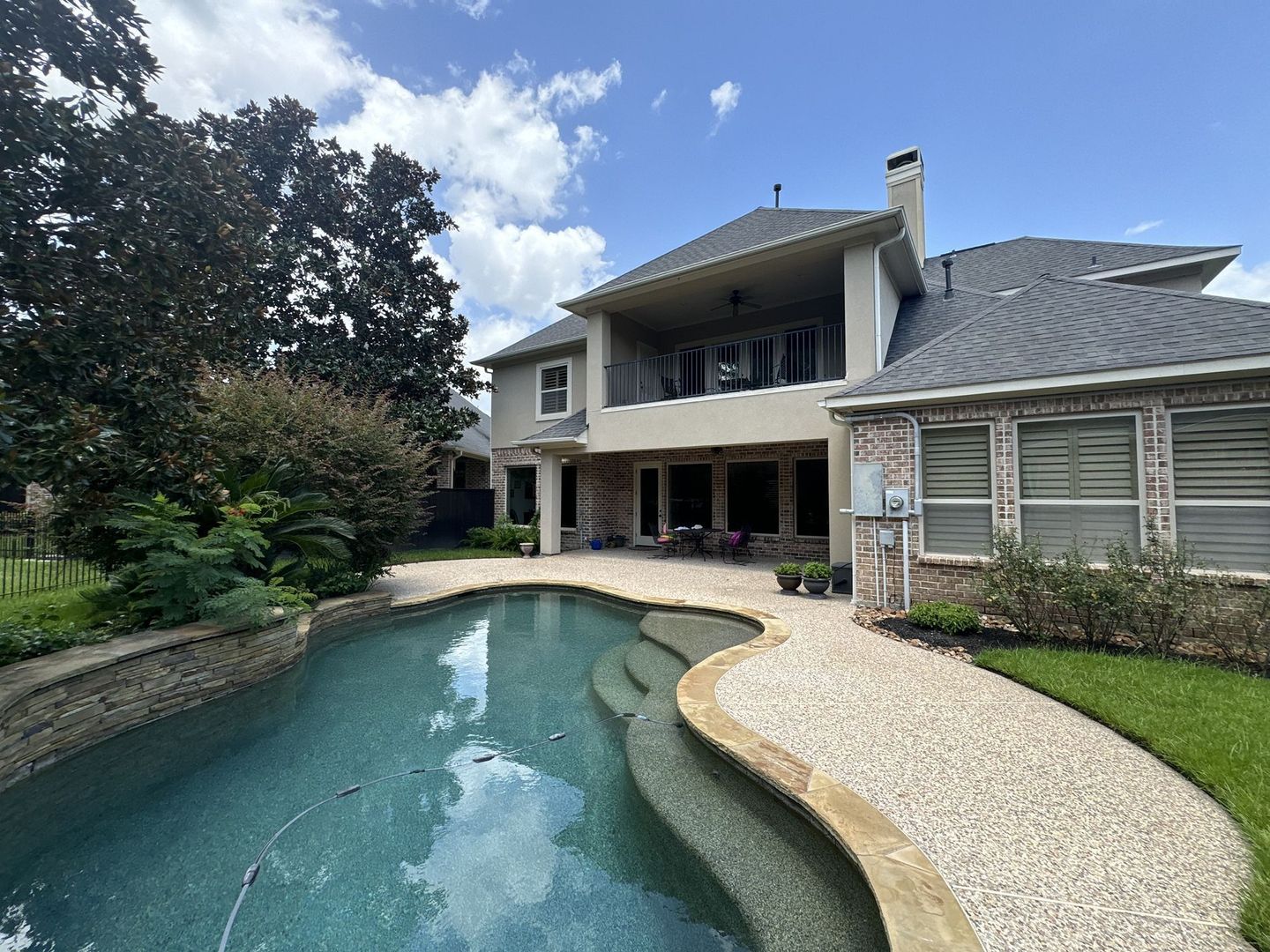 Backyard pool with a house, patio, and landscaping on a sunny day.
