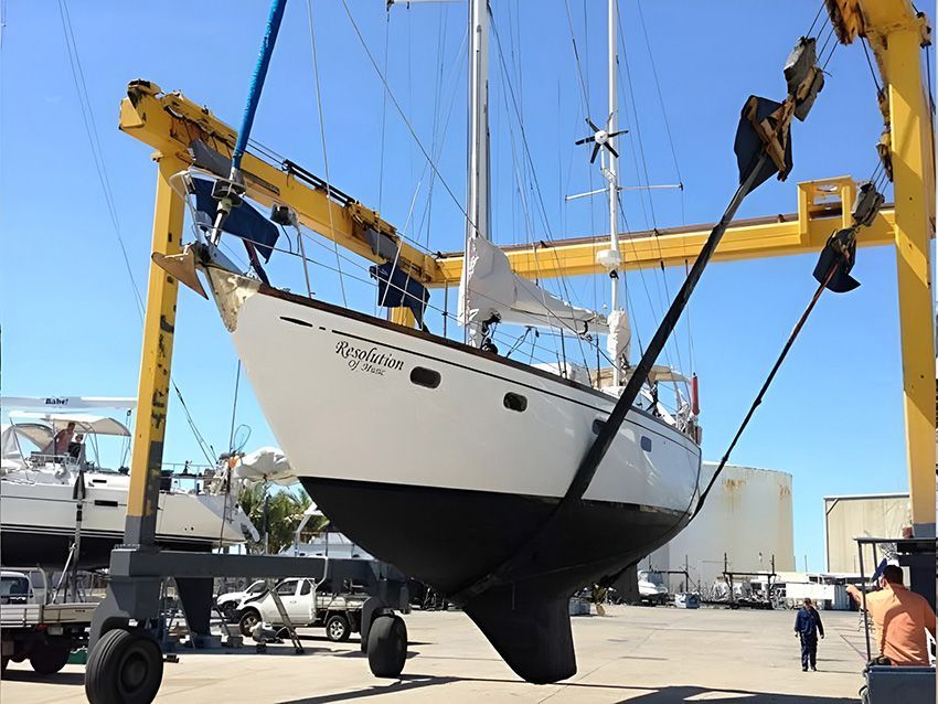 A White Sailboat is Being Lifted by a Yellow Crane ā Mackay Marine Services in Mackay, QLD