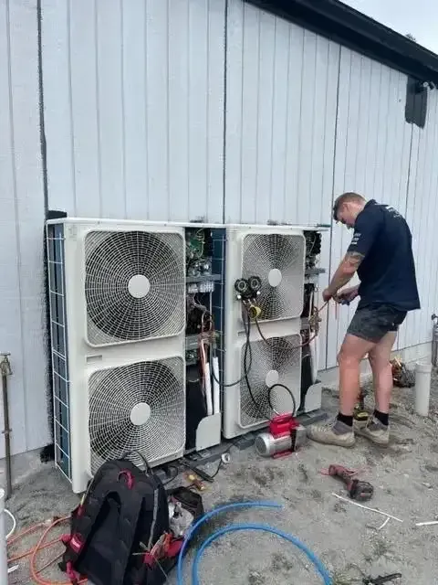 A man is working on an air conditioner outside of a building — Sparky Mid North Coast In Tuncurry, NSW