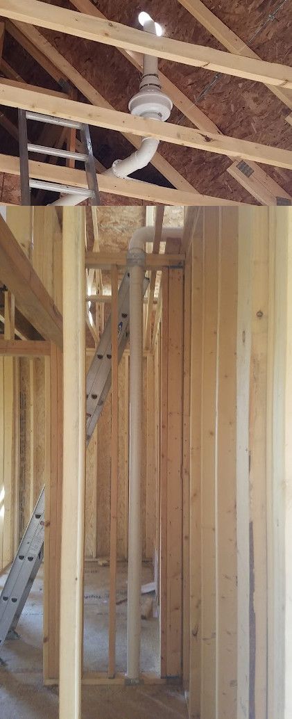 A construction site showing a vertical white PVC plumbing vent pipe running through wall studs and out through the roof.