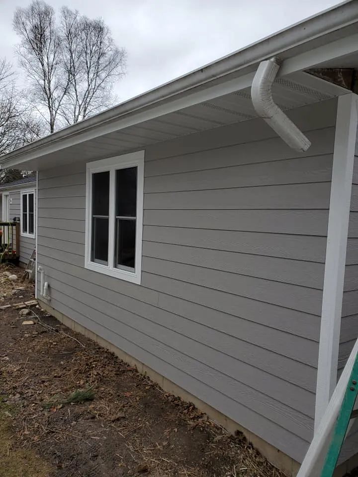 Gray house with white-framed windows, white gutter, and horizontal siding against a cloudy sky.