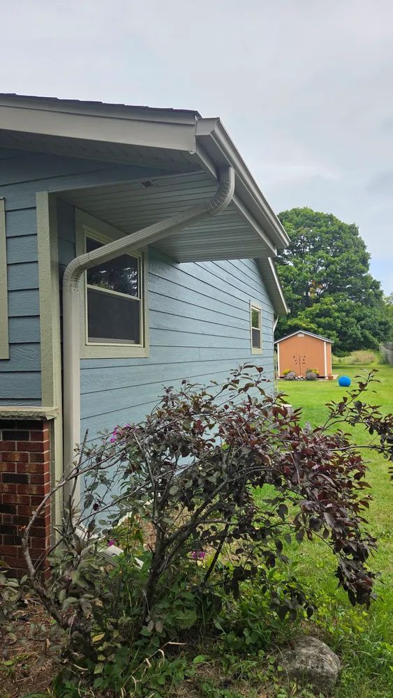Light blue house with white trim, gutters, and a small shed in the background. Overcast sky.