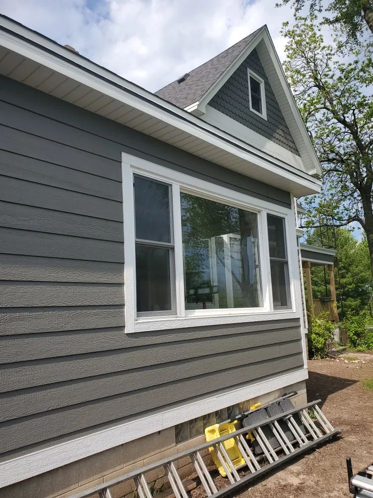 Gray house with white trim, window, and ladder on the ground.