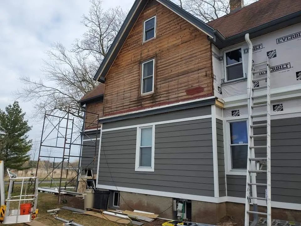 House exterior undergoing siding renovation. Brown wood and gray siding with scaffolding and ladder.