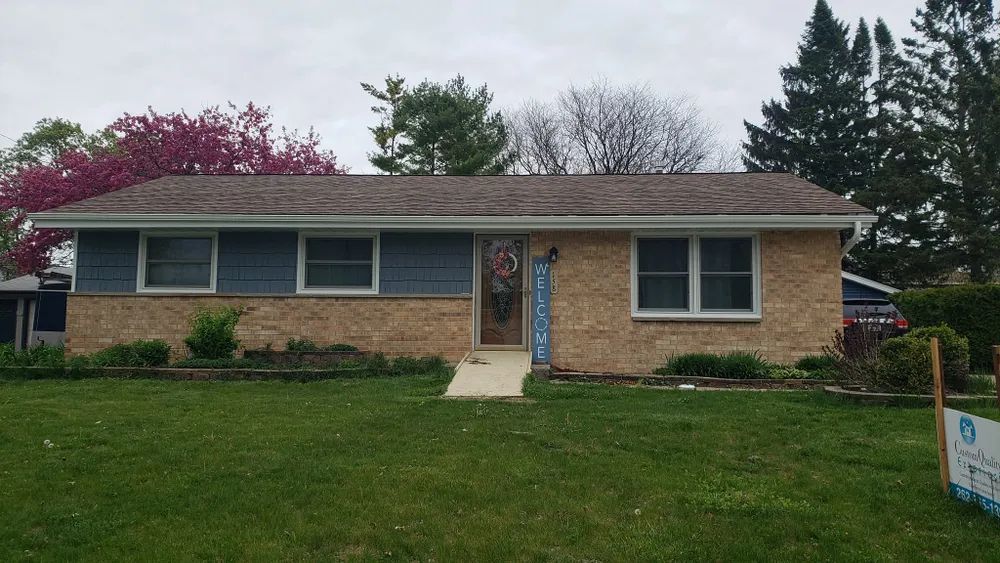 Ranch-style house with blue siding, tan brick, and a brown roof; the number 