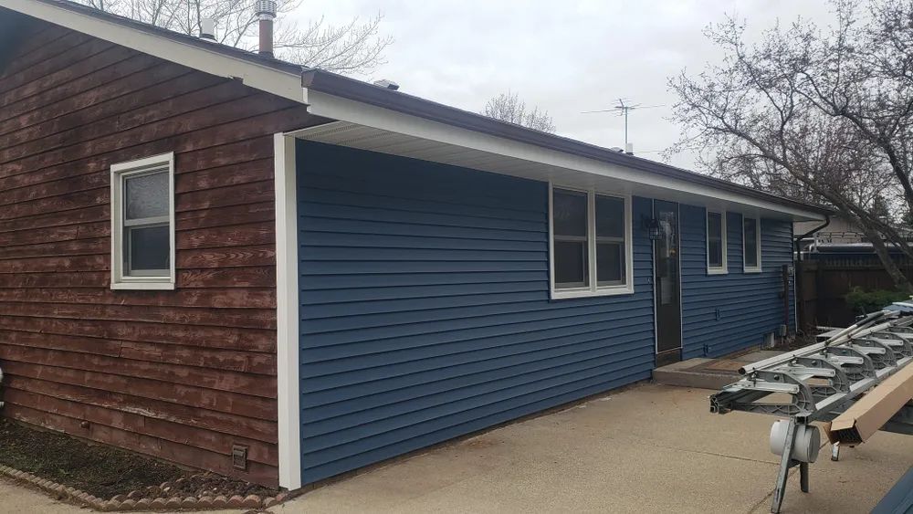 Blue siding installed on a house; brown section with a window; white trim.