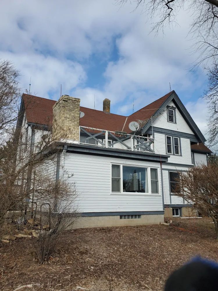 White house with brown roof, chimney, and gray trim under a partly cloudy blue sky.