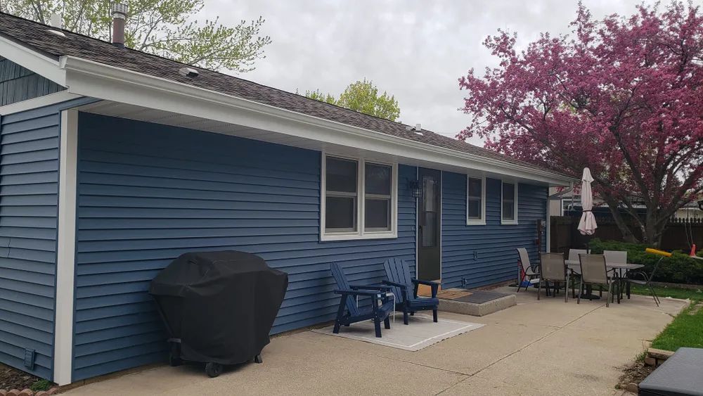 Blue house with a patio and grill, under a cloudy sky.