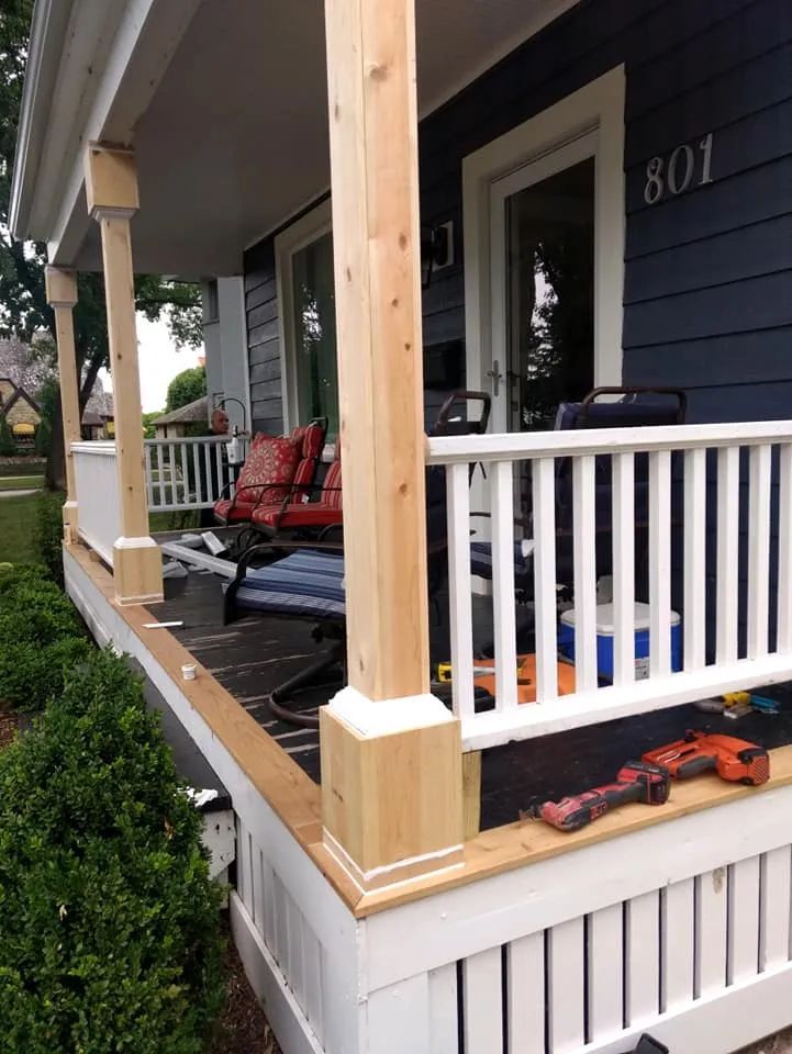 Porch with white railing and trim, wooden posts, dark blue house, and small lawn.