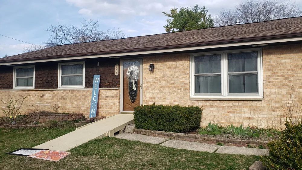 Brick house with a ramp leading to the front door. A welcome sign and bushes are in front.
