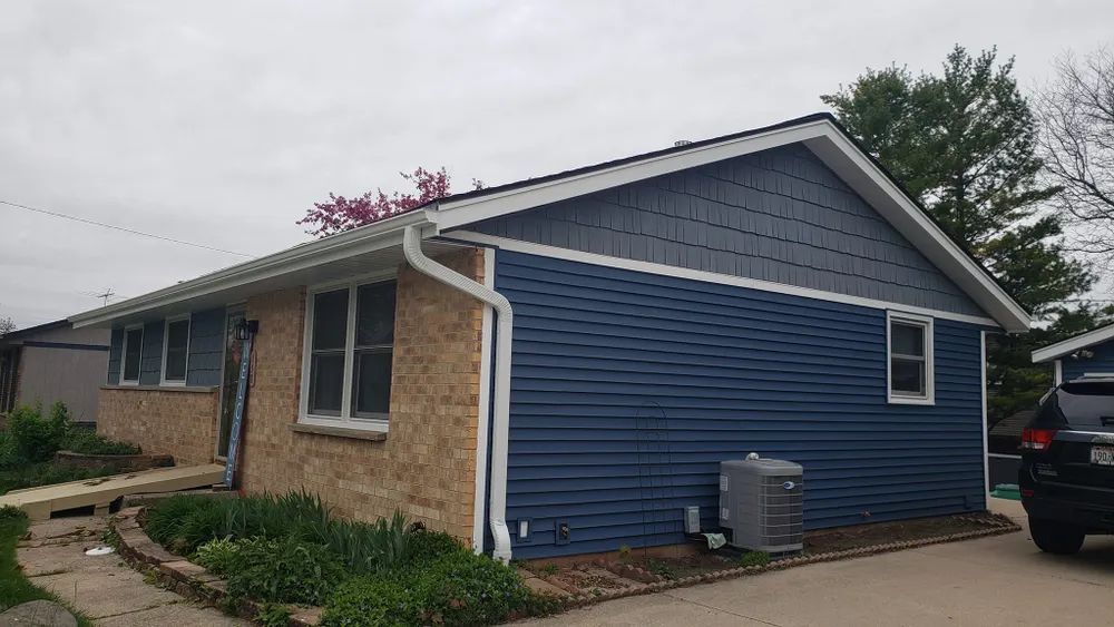 House with brick and blue siding, white trim, and a cloudy sky.