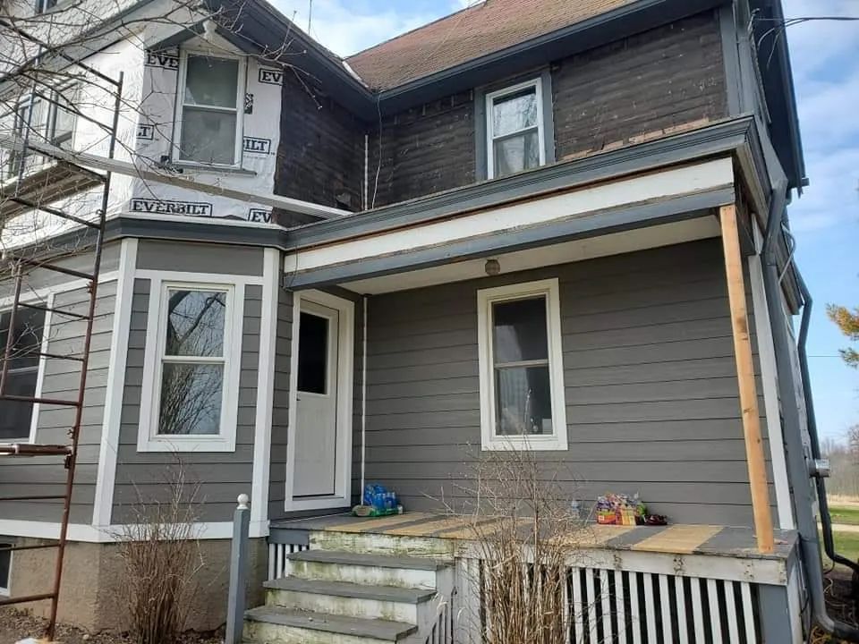 Two-story house with gray siding, white trim, and a porch under renovation, scaffolding on left.
