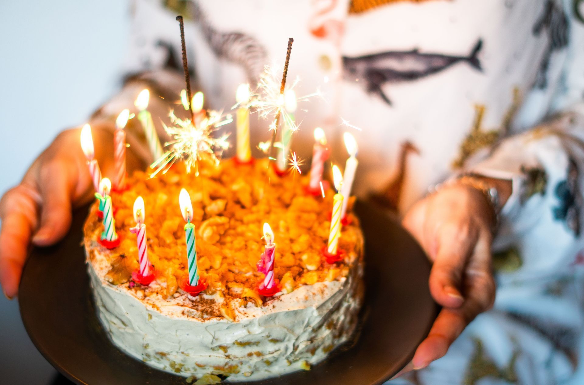 Hand holding a birthday cake with lit candles and sparklers