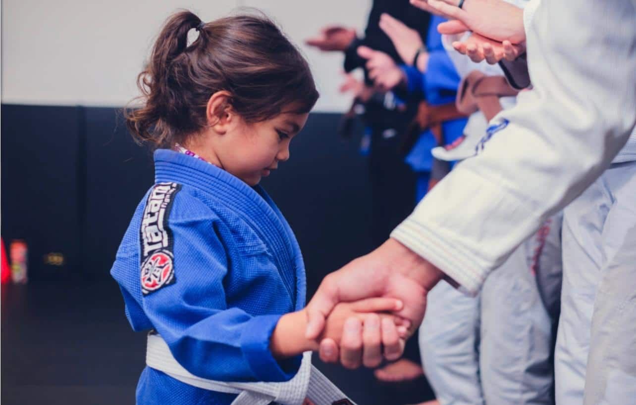 Child in a blue martial arts gi holding hands with an instructor during class