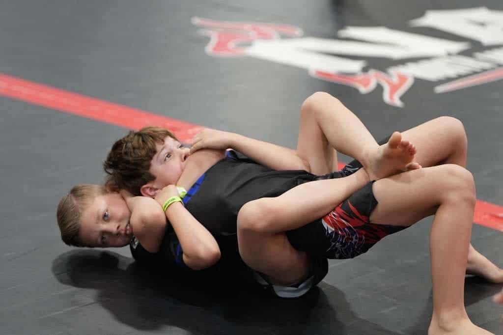 Two wrestlers grapple on a black mat, one pinning the other during a match.