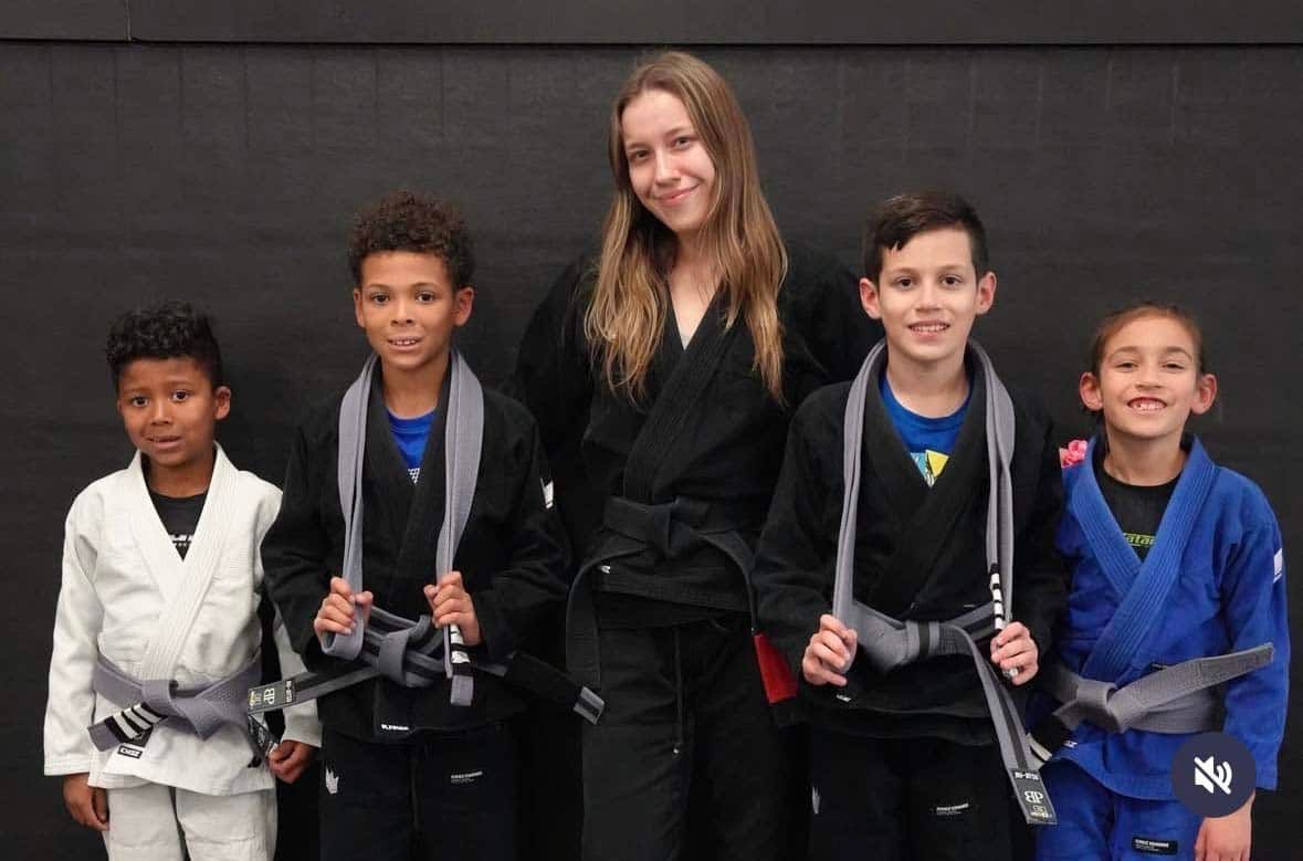 Five young jiu-jitsu competitors with medals pose with a coach in black gis.