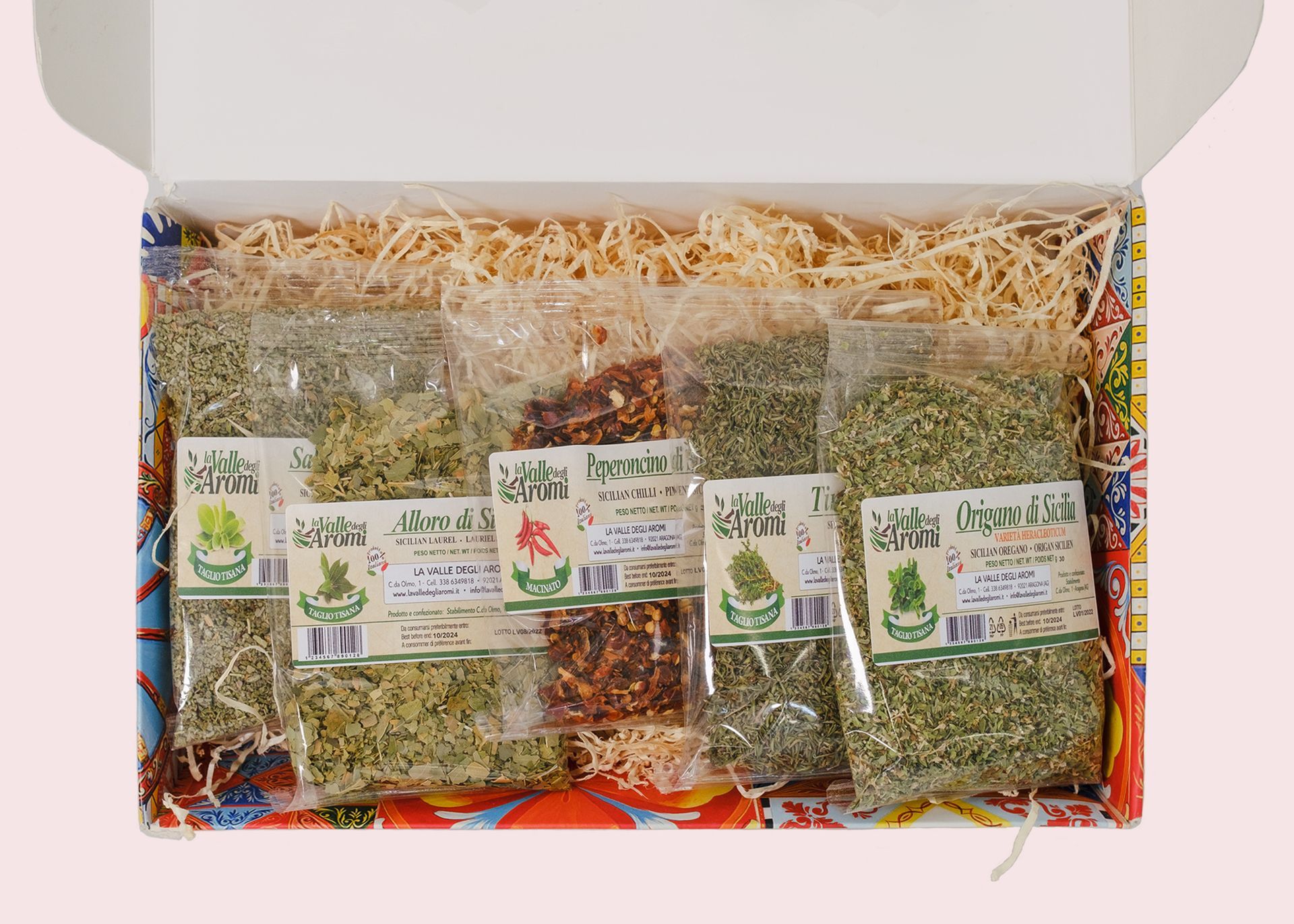 Confezione regalo aperta con tre vasetti e due bottigliette di conserve su un letto di carta sminuzzata.