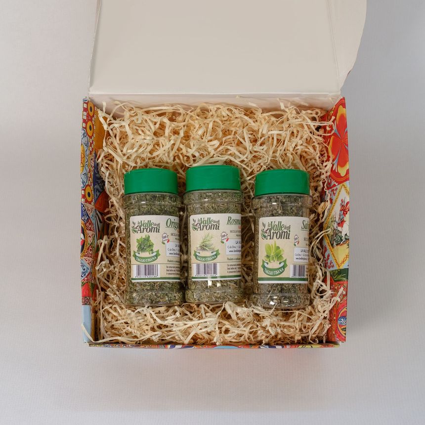 Confezione regalo aperta con tre vasetti e due bottigliette di conserve su un letto di carta sminuzzata.