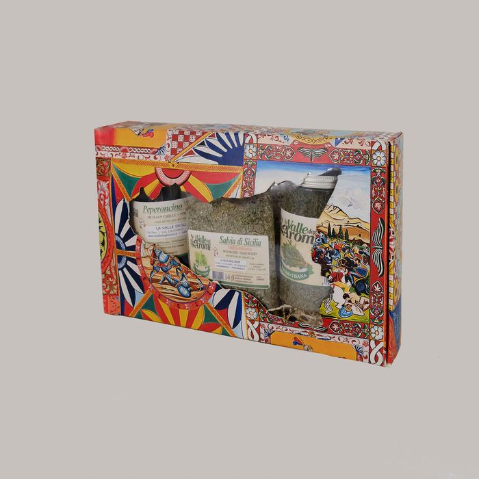 Confezione regalo aperta con tre vasetti e due bottigliette di conserve su un letto di carta sminuzzata.